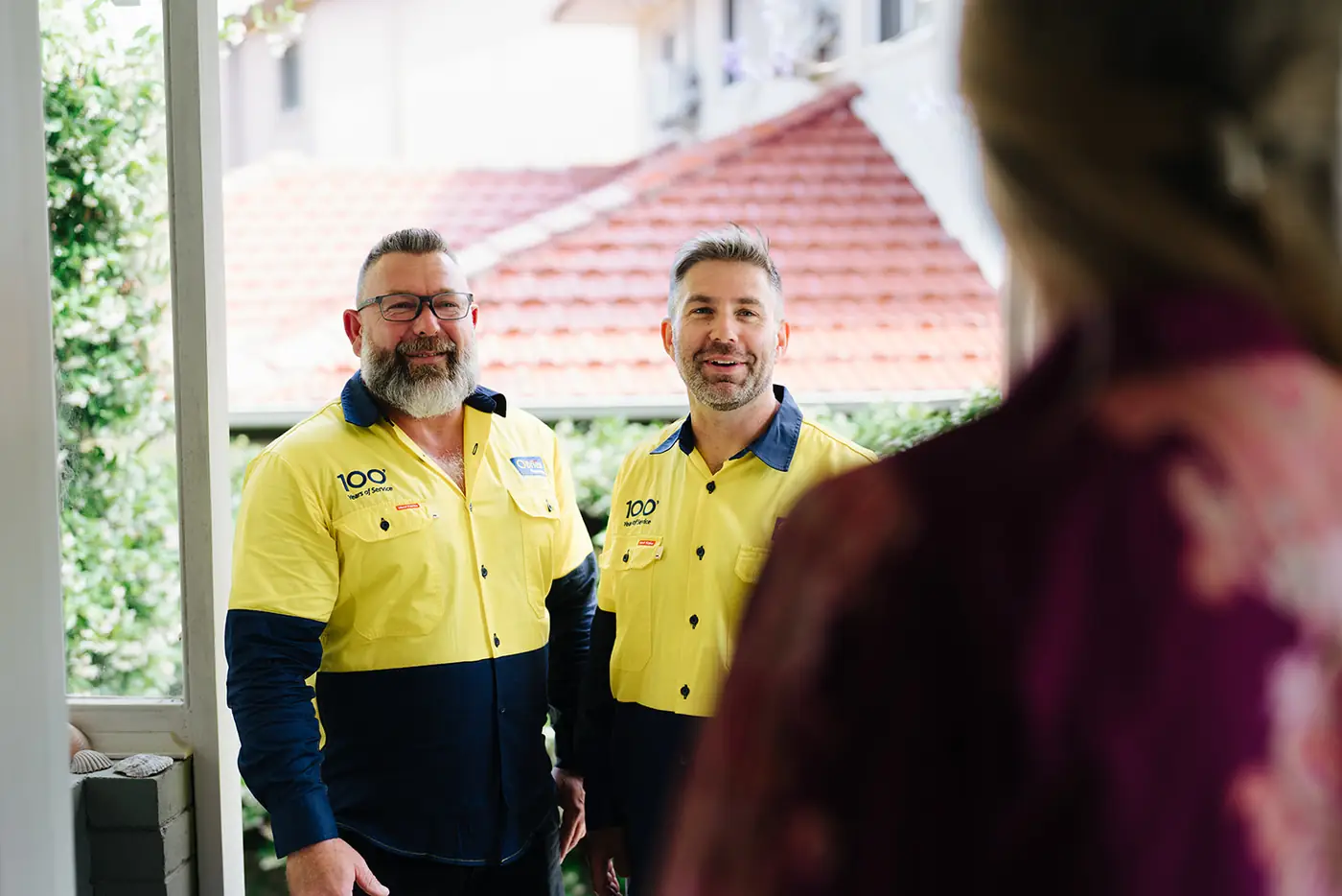 Two O'Brien plumbers greeting a customer at her front door